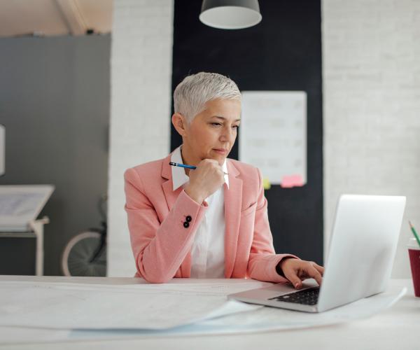 Older businesswoman sitting at desk in front of a laptop in an office