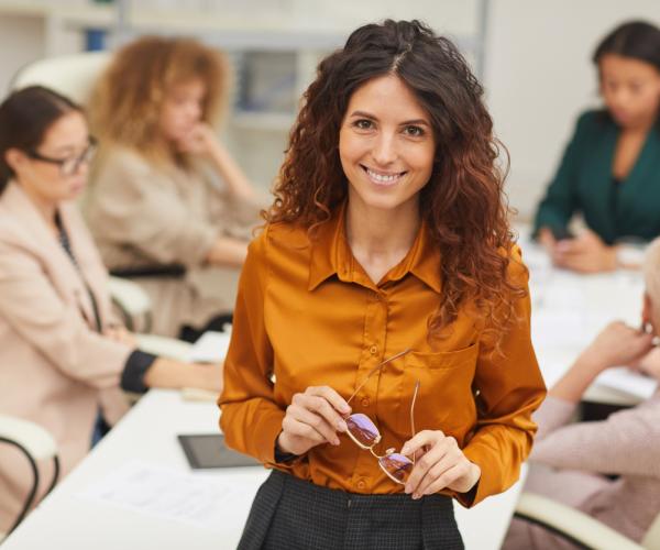 Woman standing with with eyeglasses taken off looking at camera smiling with colleagues