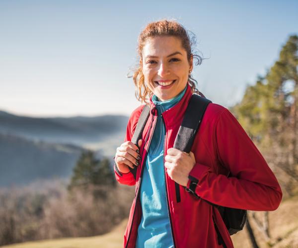 Brunette haired woman with backpack on in front of mountain range