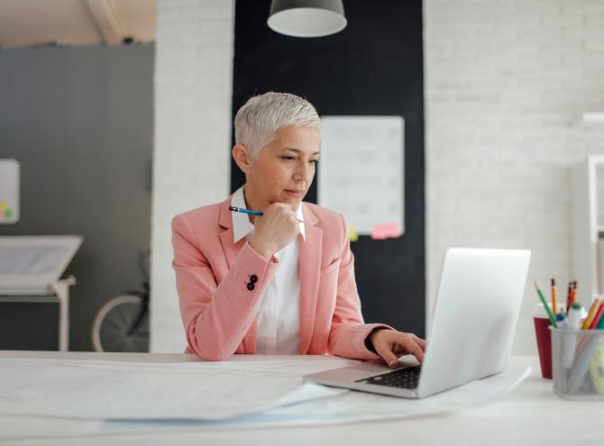 Older businesswoman sitting at desk in front of a laptop in an office