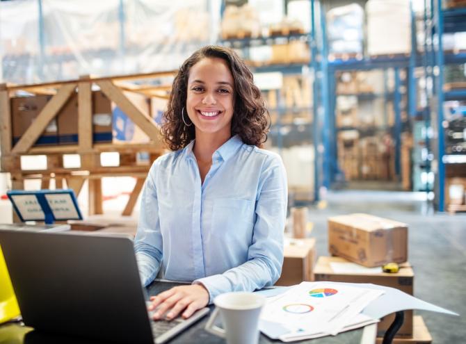 Business woman working on laptop at a warehouse.