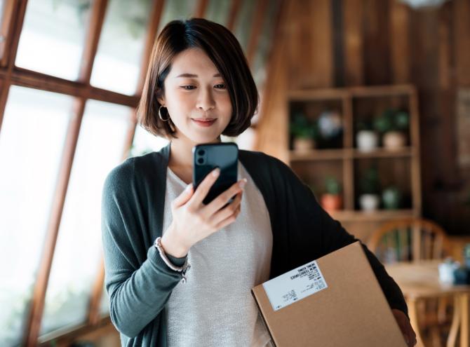 Woman looking at smartphone holding a package. 