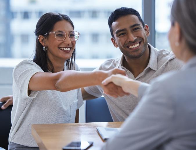 Young man and woman meeting with a banker and shaking hands