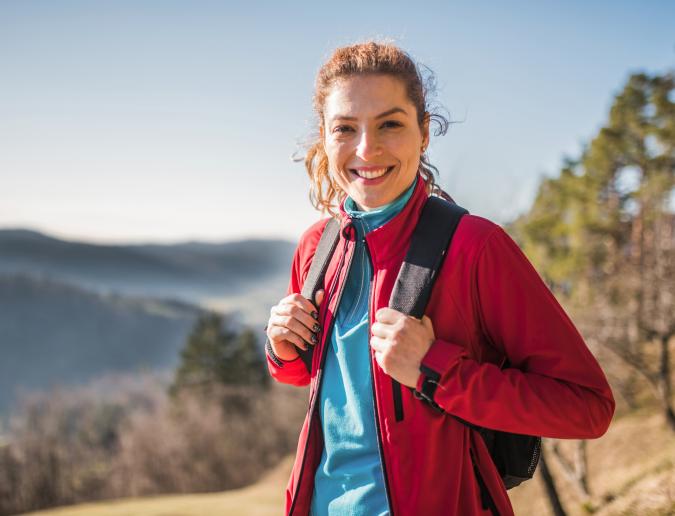 Brunette haired woman with backpack on in front of mountain range